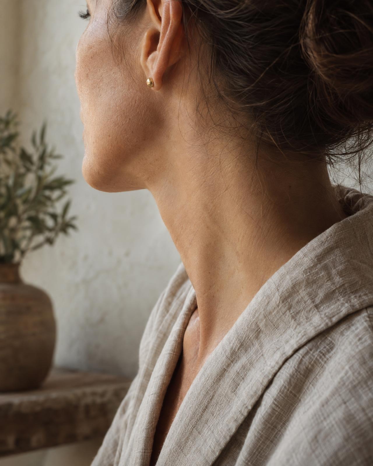 A woman's jaw and neck in soft window light, wearing a linen robe
